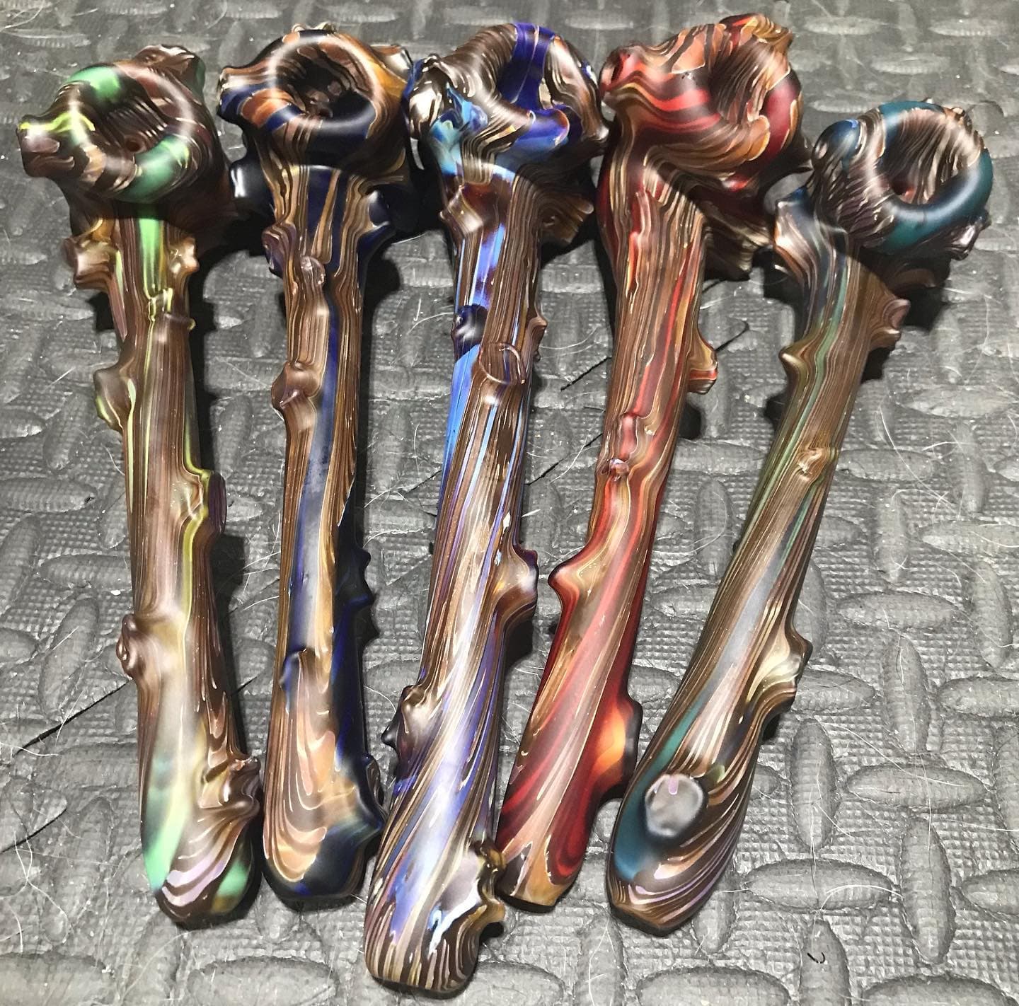 Five branch-textured dry pipes on a garage floor mat, bark-like surfaces with color running through the grain.