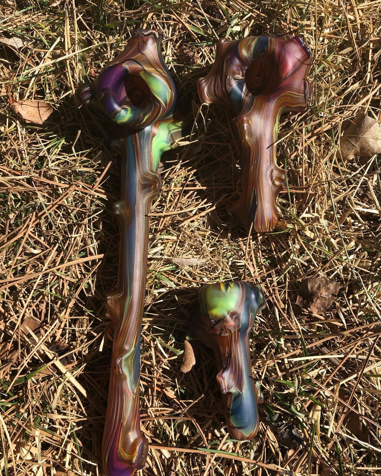 A long branch-textured Gandolf beside a Sherlock and a compact hand pipe on dry grass.