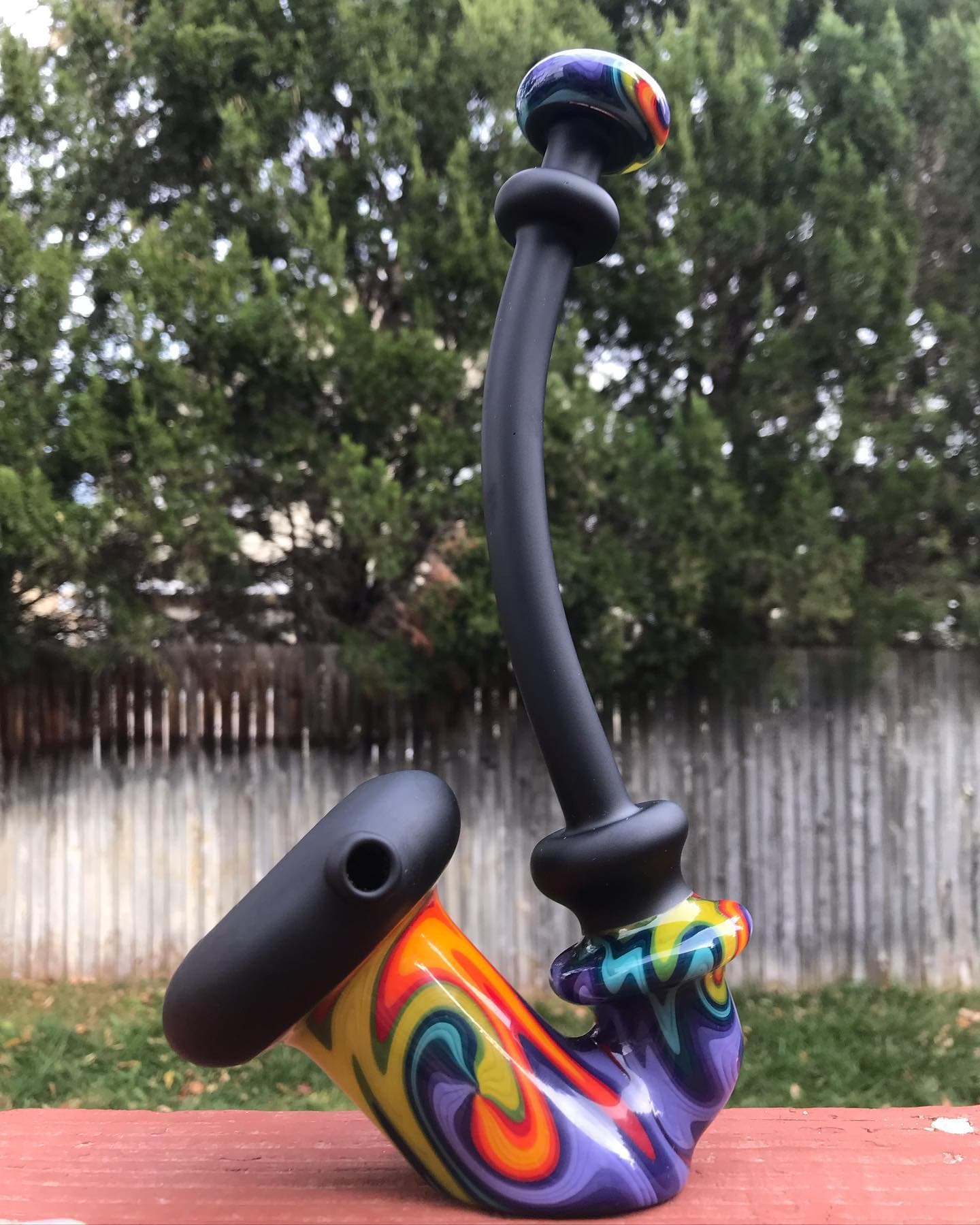 An elongated matte-black Sherlock with vivid color at the base and mouthpiece, standing on a deck rail.