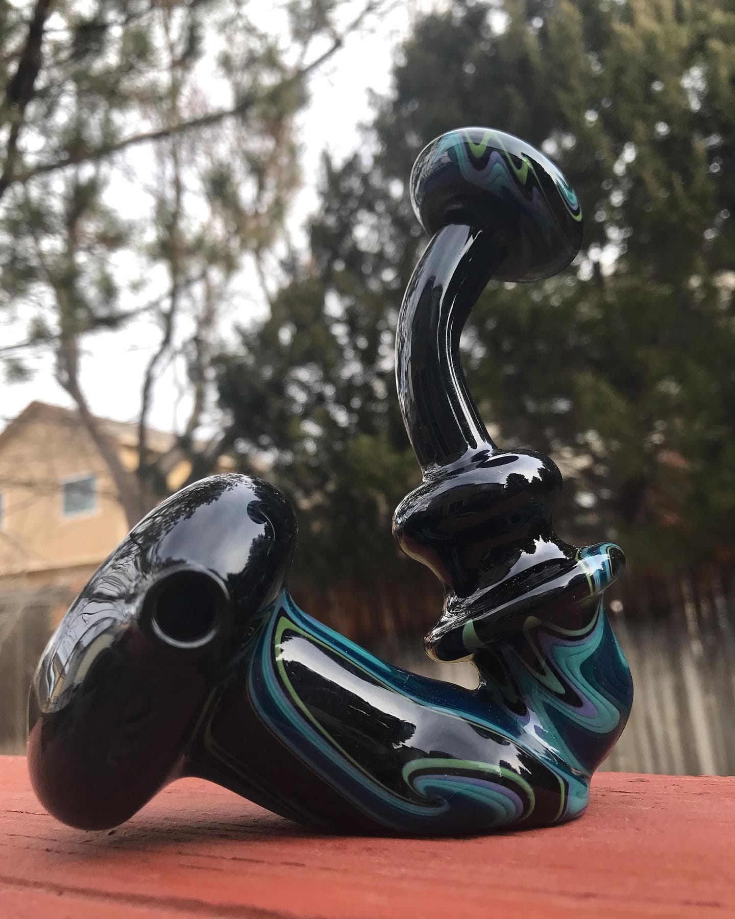 A hammer-style bubbler in glossy black glass with teal, green, and lavender swirl work.