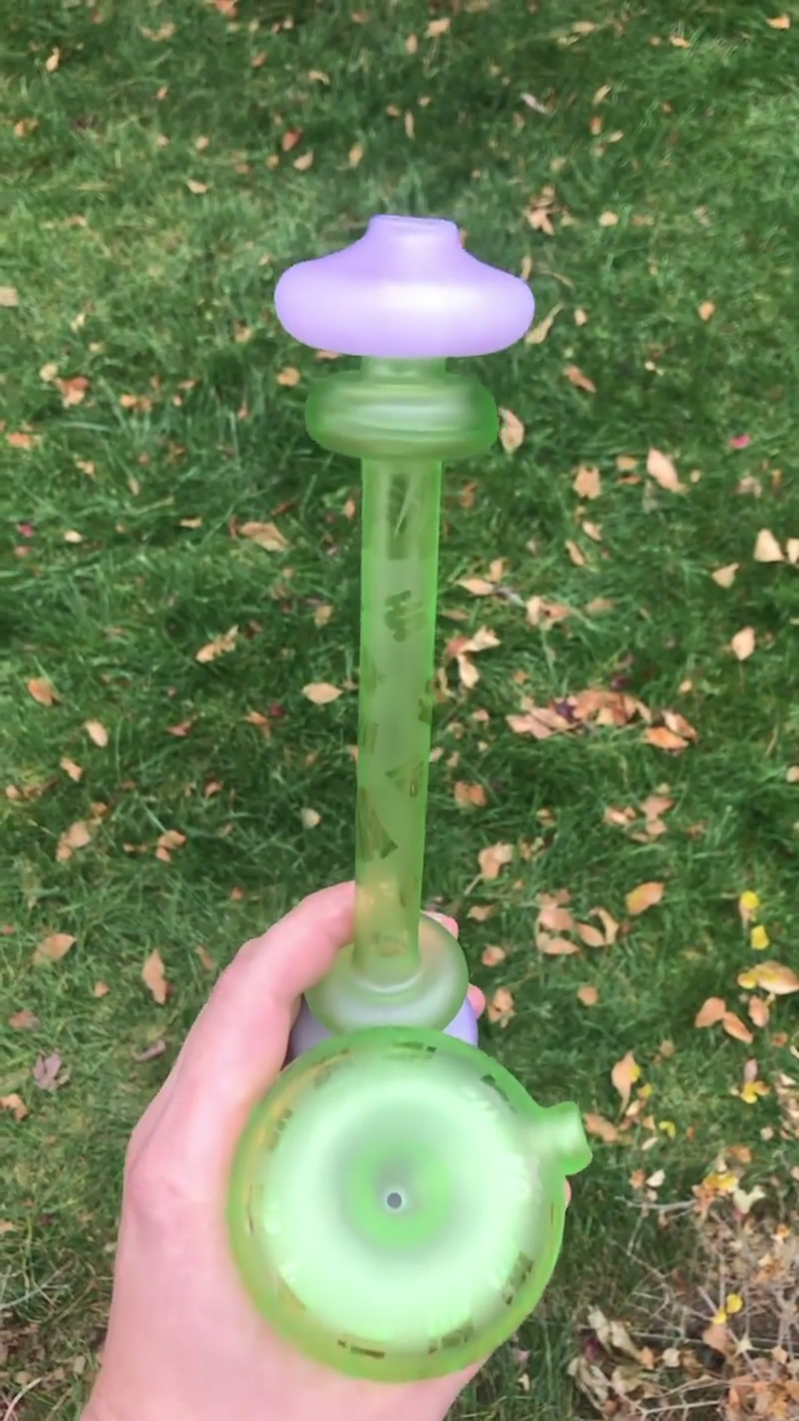 A slender frosted lime-green water piece with a lavender cap, held over a lawn.
