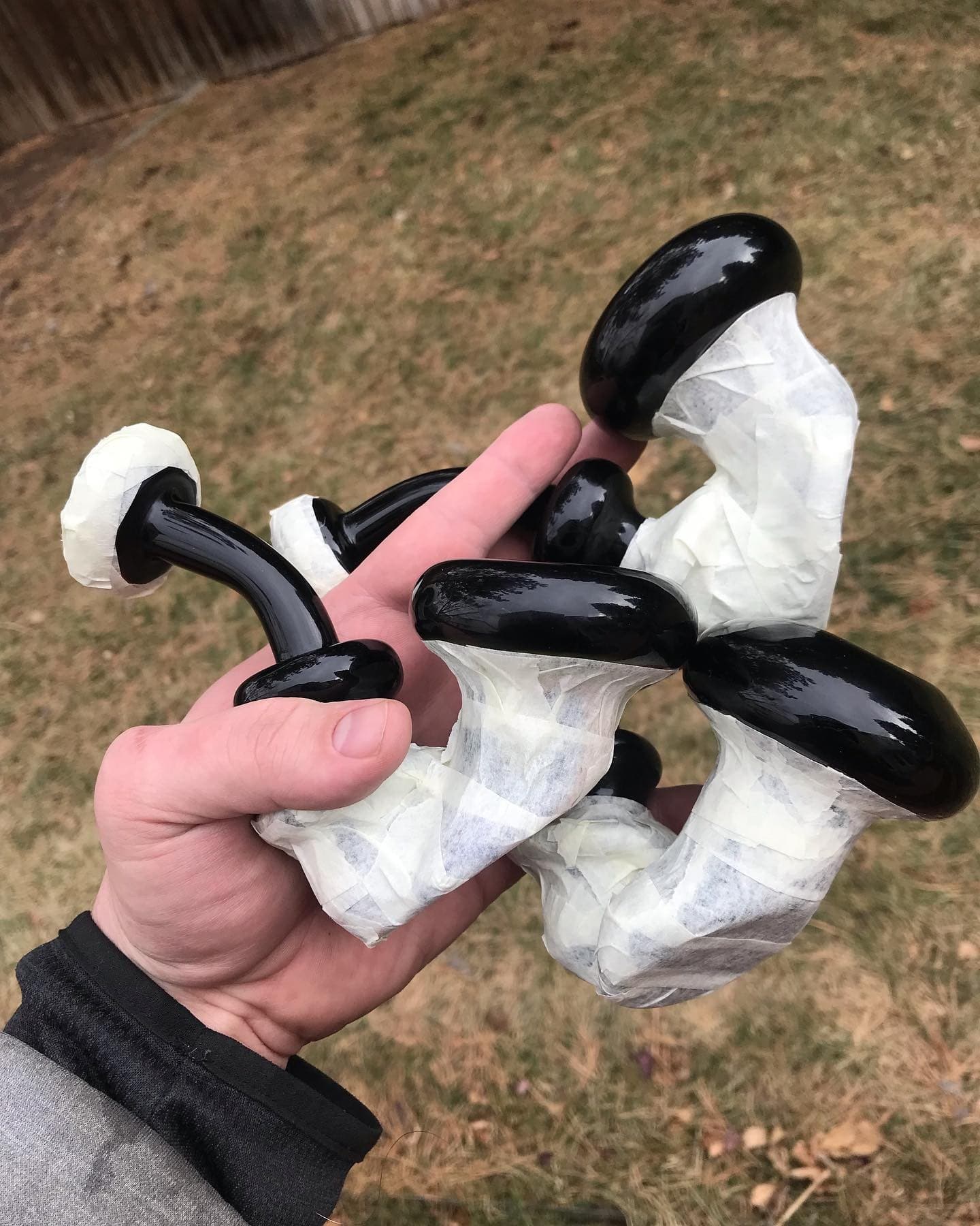 Joe’s hand holding a cluster of black glass pieces wrapped in masking tape, mid-process.