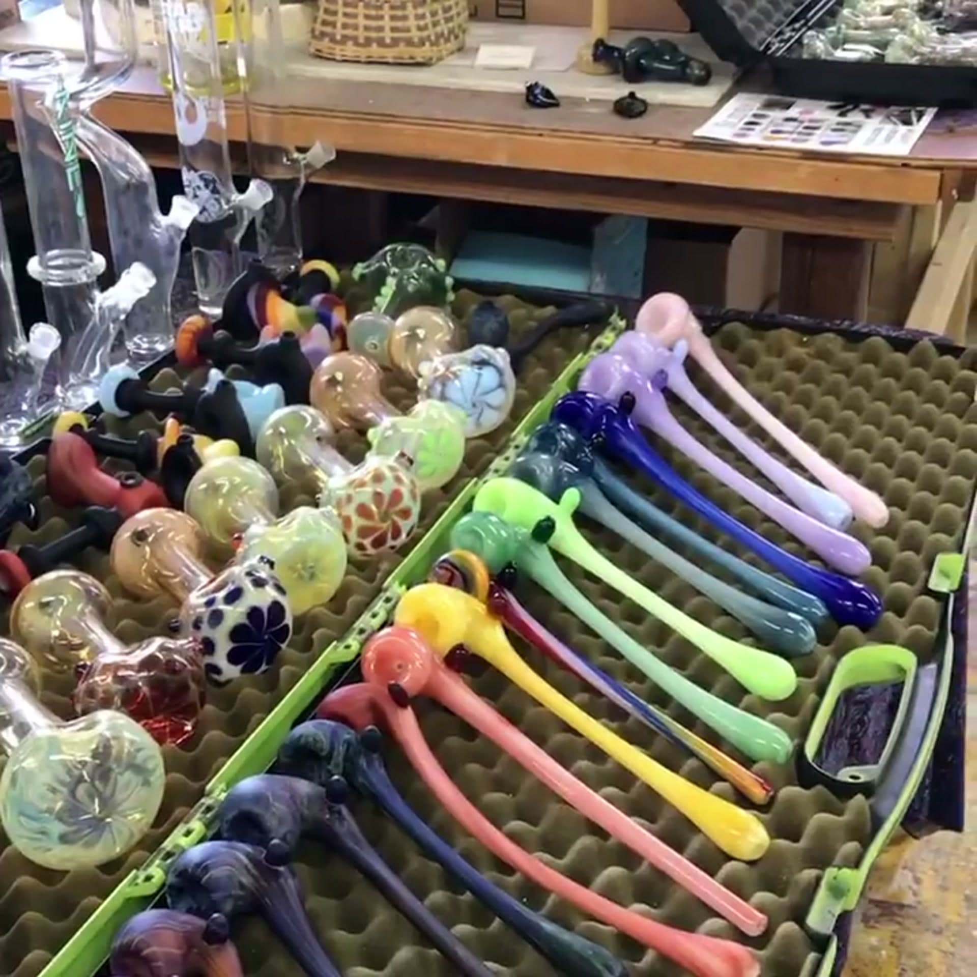 A foam-lined case of finished Gandolfs and hand pipes on Joe’s workbench, with water pieces standing behind.