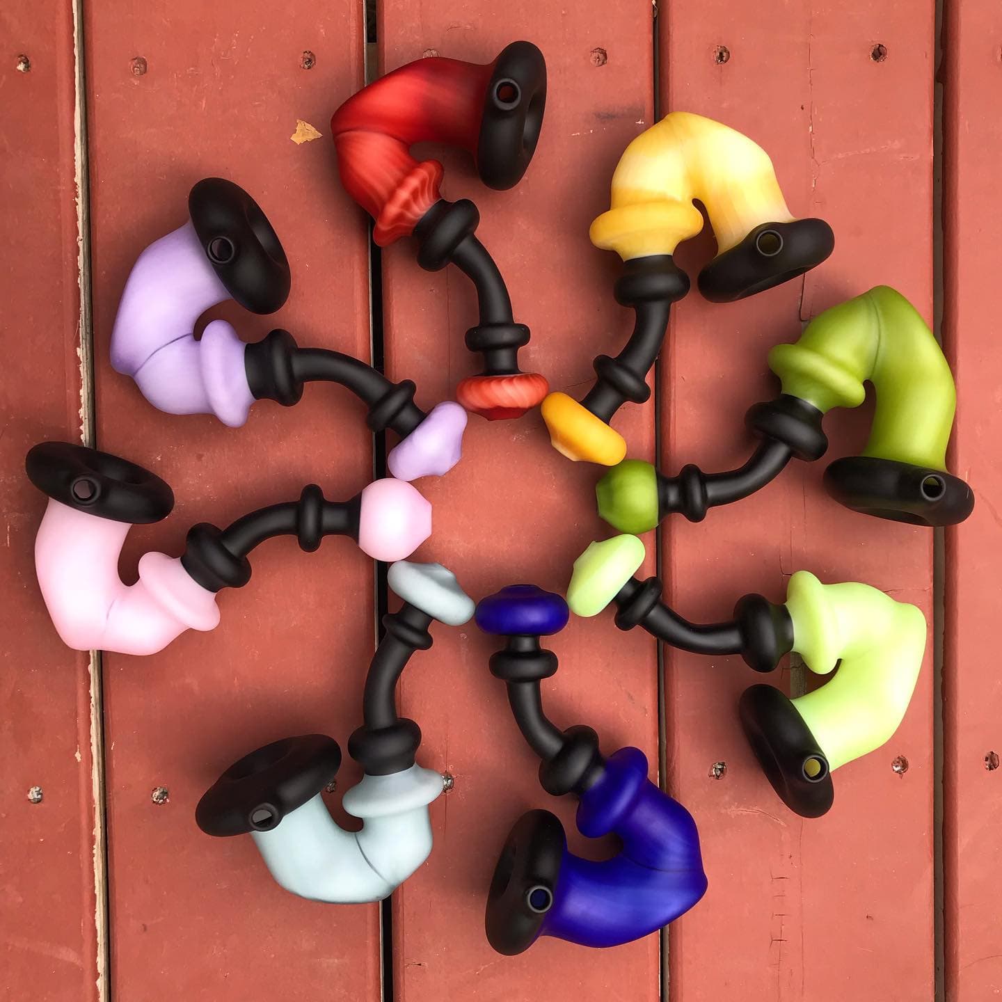 Eight satin-finish Sherlock-style pipes arranged in a circle by color on a wooden deck.