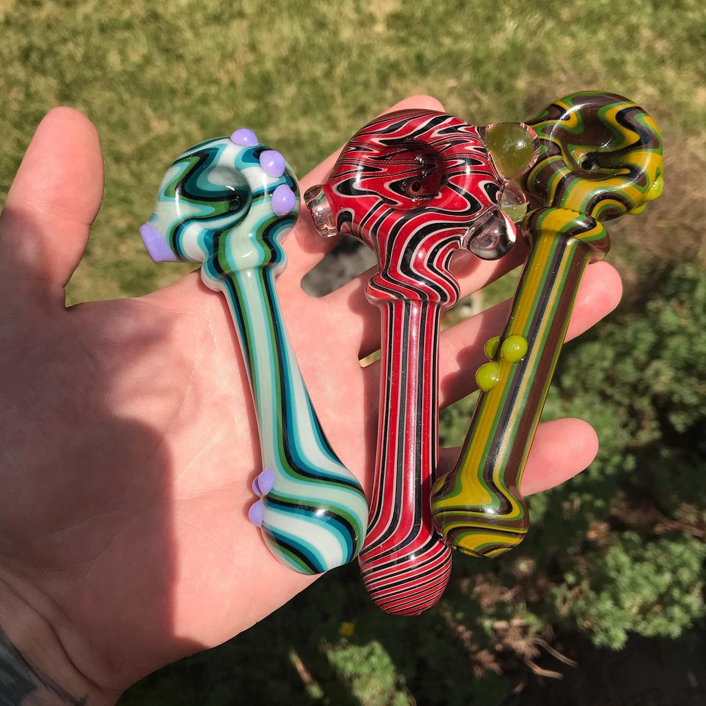 Three compact dry hand pipes held in a palm, each with different color and pattern.