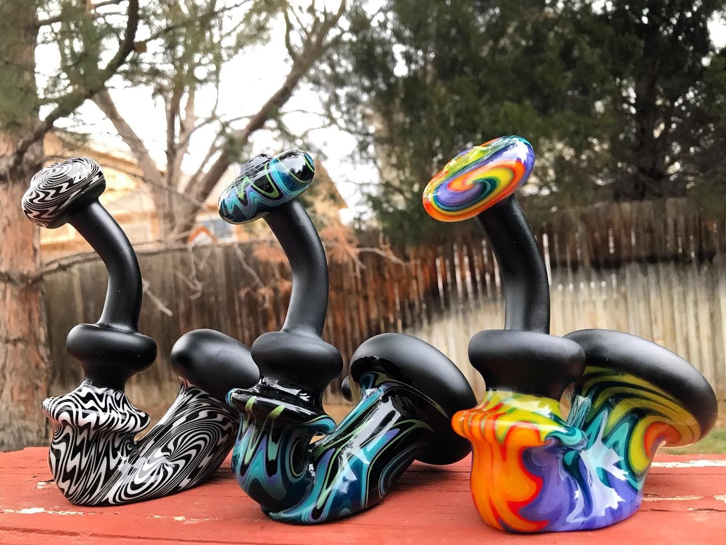 Three Sherlock-style pipes on a wooden deck, matte black with colored swirl sections.