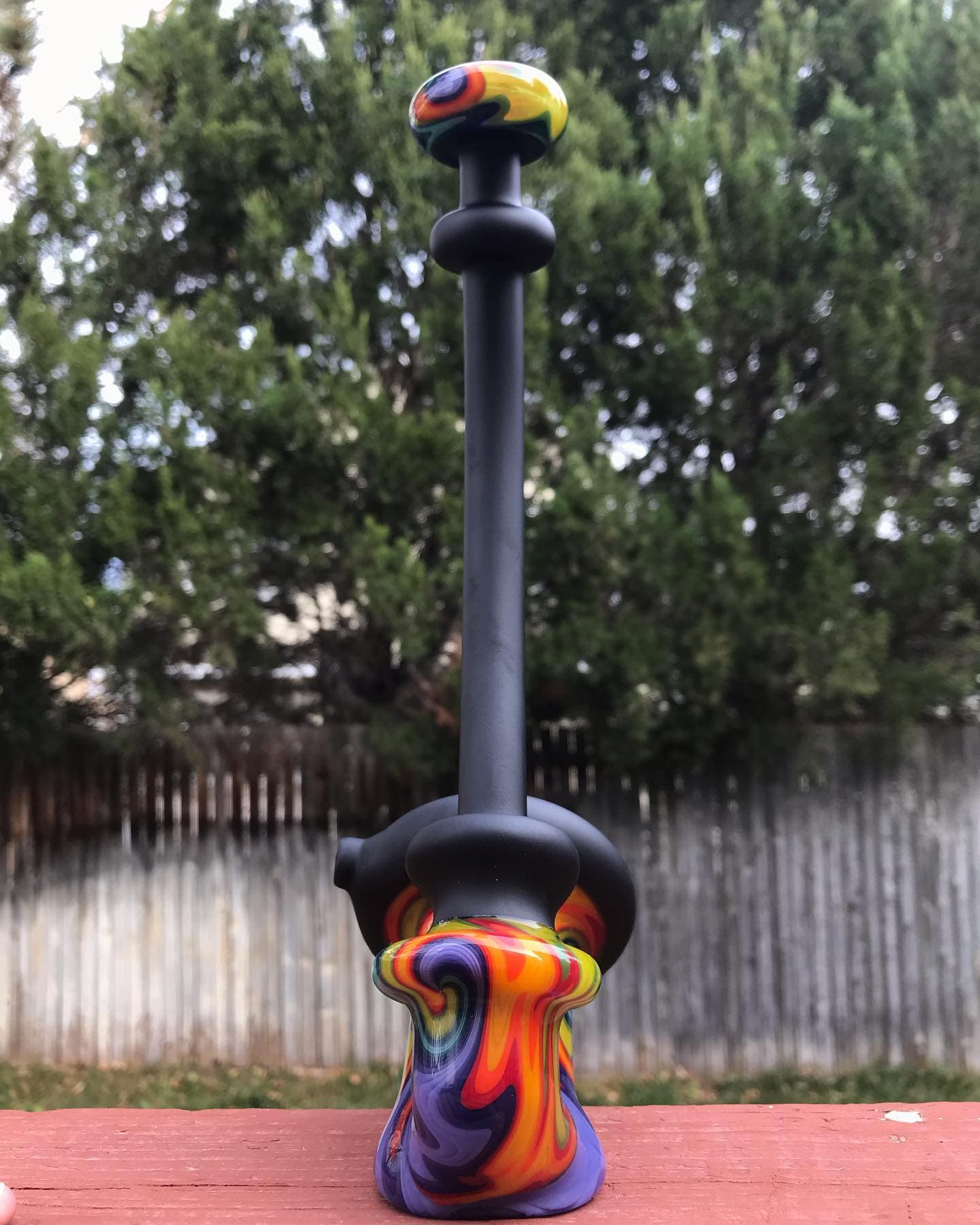 A tall matte-black water pipe with colorful swirl glass at the foot and mouthpiece.