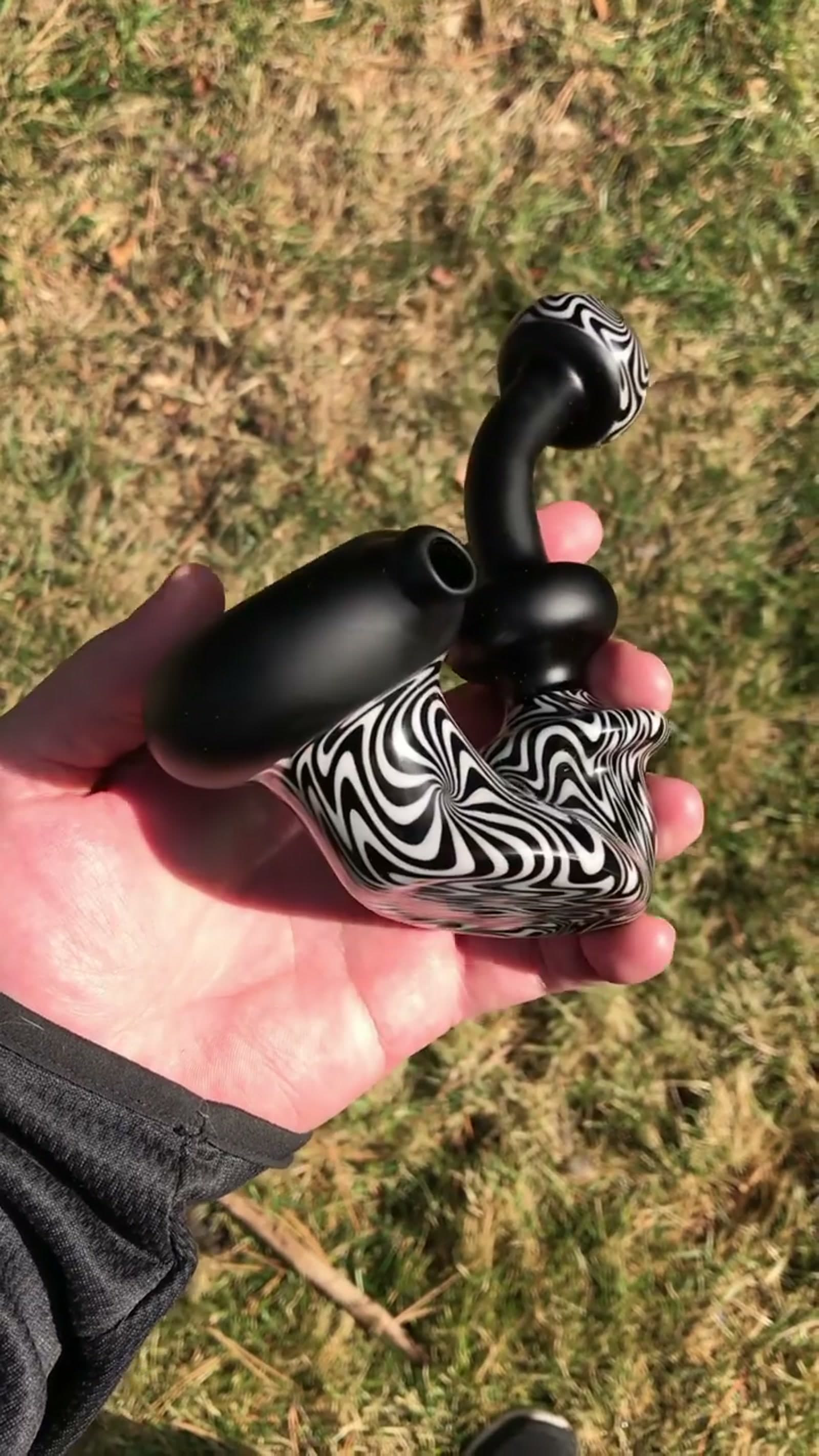 A compact bubbler with dense black-and-white wig-wag at the base, held over grass.