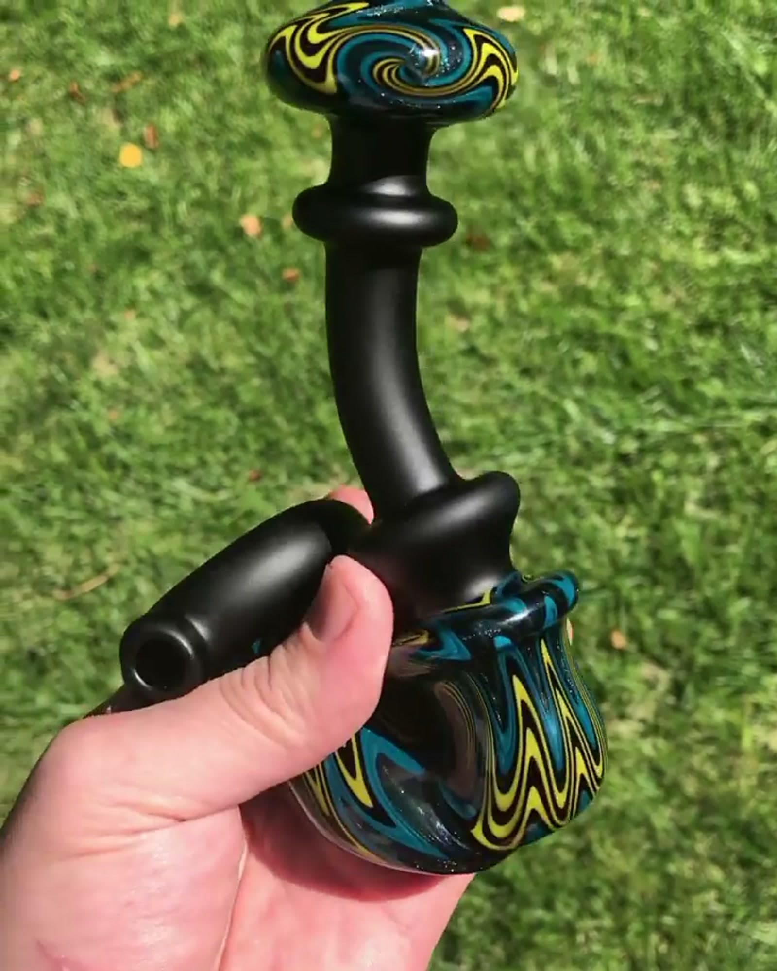 A compact piece combining tight colorful wig-wag with a matte black stem, held outdoors.